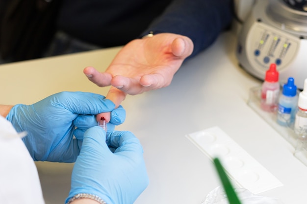 Médecin prenant un test sanguin du doigt du patient dans un tube à essai en laboratoire