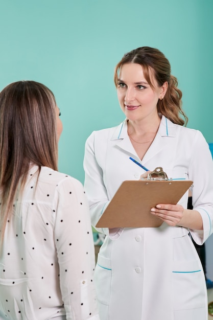 Médecin avec presse-papiers et jeune patiente debout dans le hall de la clinique moderne