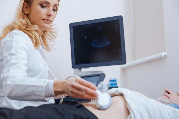 Médecin professionnel concentré positif travaillant dans le tout en fournissant un balayage ultrasonique de l'abdomen et en utilisant une machine à ultrasons