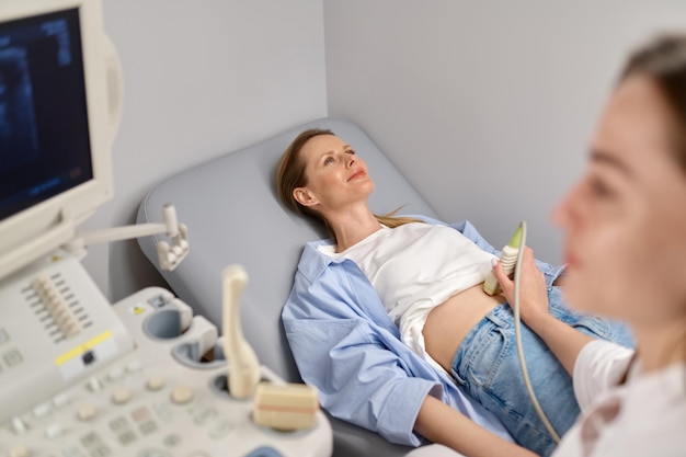 Médecin professionnel examinant son patient en train de faire une échographie abdominale à l'aide d'un appareil de scanner sonogramme. Concept de confirmation de grossesse précoce