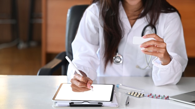 Médecin professionnel en uniforme médical travaillant avec une tablette numérique dans une clinique médicale.