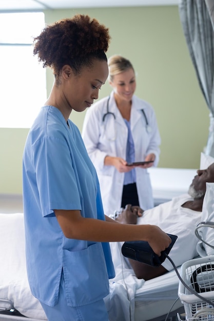 Photo médecin de race mixte dans la chambre du patient se préparant à vérifier la tension artérielle d'un patient de sexe masculin