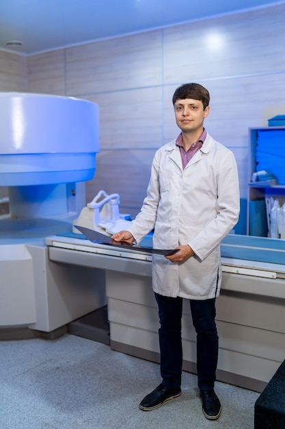 Médecin radiologue compétent avec image radiographique dans les mains. Machine CT sur fond.