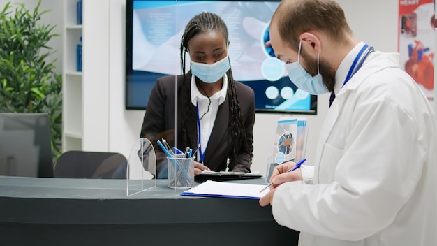 Photo médecin et réceptionniste parlant de rendez-vous à la réception de l'hôpital, se préparant à assister à un examen de contrôle pendant la pandémie de coronavirus. personnes travaillant dans un établissement médical.