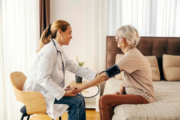 Un médecin rend visite à une femme âgée à la maison et mesure sa tension artérielle.