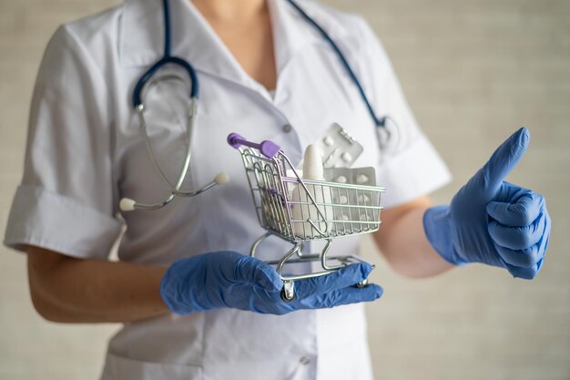 Un médecin sans visage avec une blouse médicale et un stéthoscope tient un petit panier plein de médicaments Concept de pharmacie Le pharmacien montre un pouce vers le haut