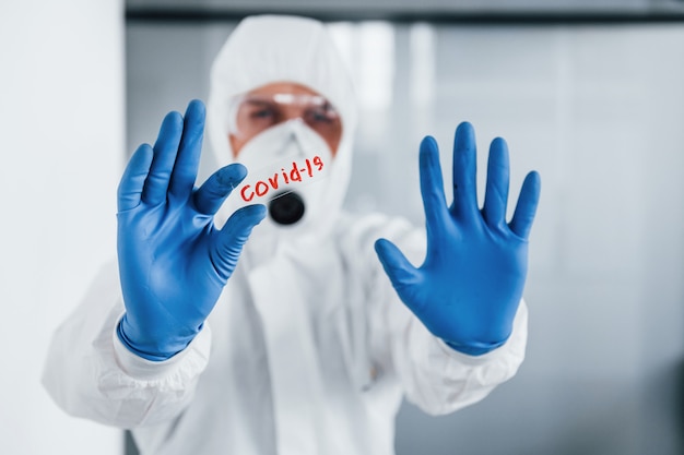 Photo médecin scientifique masculin en blouse de laboratoire, lunettes et masque de défense détient le verre avec le mot covid-19 dessus