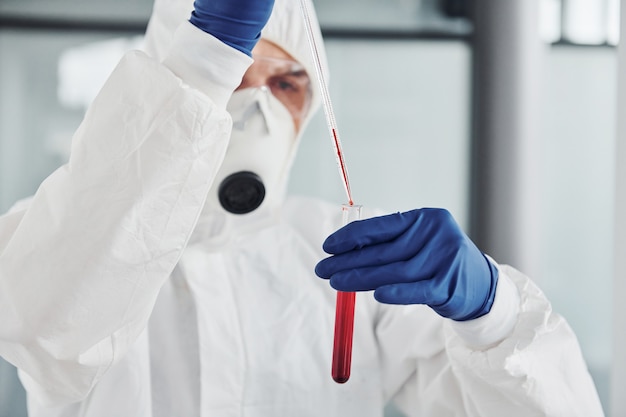 Médecin scientifique masculin en blouse de laboratoire, lunettes et masque de défense fonctionne avec un tube à essai avec du sang à l'intérieur