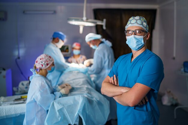 Le médecin se croise dans un masque médical. Équipe médicale en arrière-plan. Médecin à lunettes avec masque médical sur le visage. Photo en gros plan.