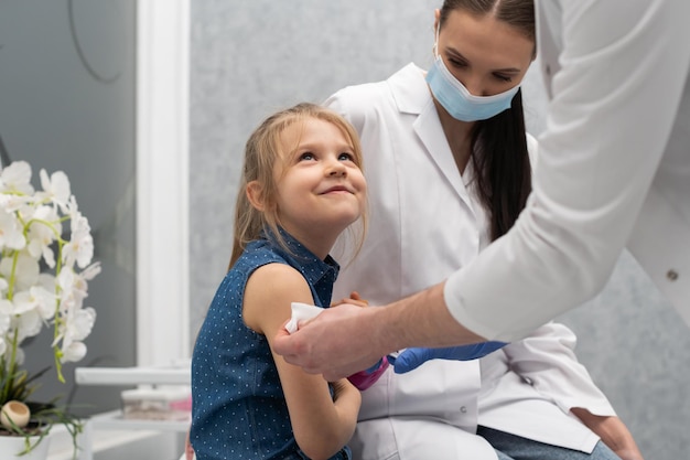 Le médecin se prépare à vacciner une petite fille Une jeune infirmière s'assoit à côté de l'enfant pour faire en sorte que l'enfant se sente en sécurité Vaccin préventif pour les jeunes enfants