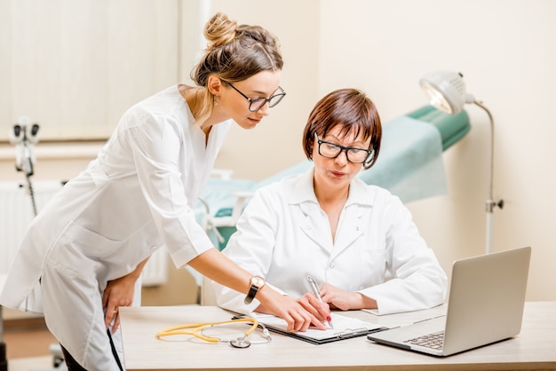 Médecin senior et assistante de jeune femme travaillant avec un ordinateur portable et des documents au cabinet gynécologique