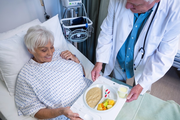 Médecin servant le petit déjeuner et la médecine au patient senior