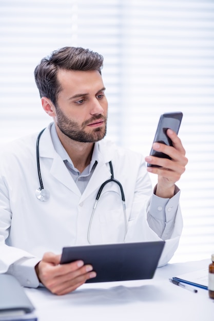 Médecin De Sexe Masculin à L'aide De Téléphone Portable Tout En Tenant La Tablette Numérique