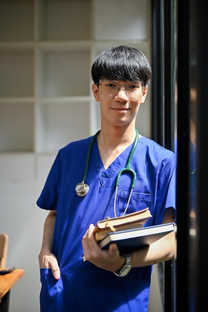 Un médecin de sexe masculin asiatique en gommages et lunettes se tient dans le couloir de l'hôpital avec des livres