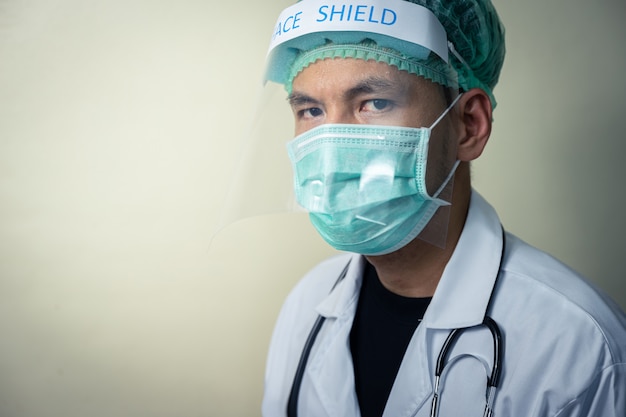 Photo médecin de sexe masculin asiatique portant un écran facial et uniforme avec stéthoscope