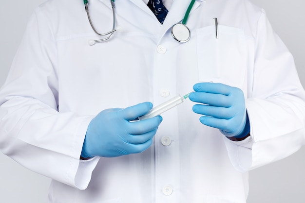 Médecin de sexe masculin dans une blouse blanche et cravate se dresse et détient une seringue en plastique avec une aiguille, portant des gants médicaux stériles bleus