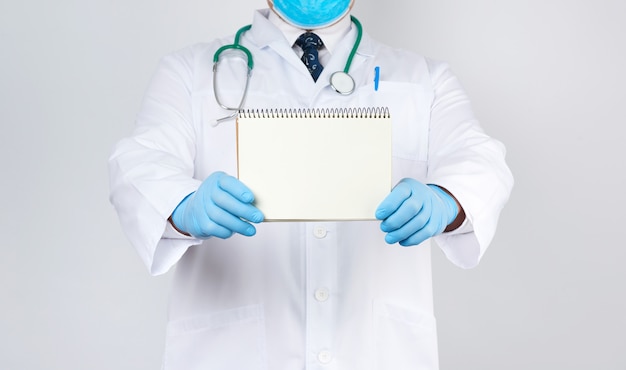 Médecin de sexe masculin dans une blouse blanche et des gants bleus médicaux est titulaire d'un cahier avec des draps blancs vierges