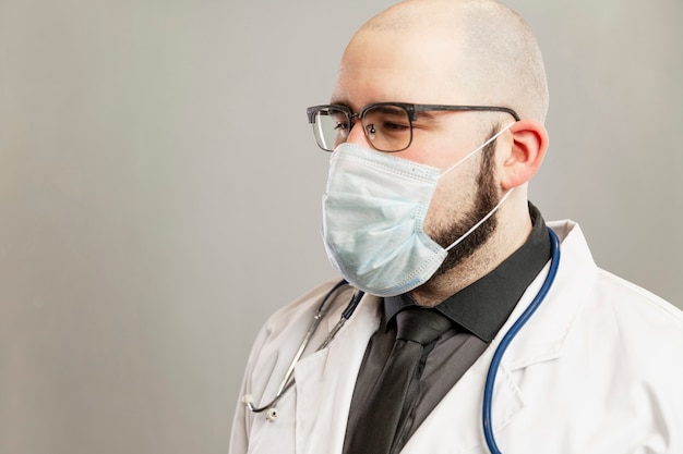 Médecin de sexe masculin dans une blouse blanche et un masque médical. Mur gris.