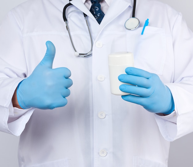 Médecin de sexe masculin dans une blouse médicale blanche et des gants en latex bleu est titulaire d'un pot de pilules en plastique blanc