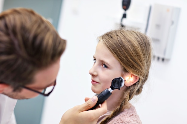 Médecin de sexe masculin examinant l'oreille de la fille avec un otoscope