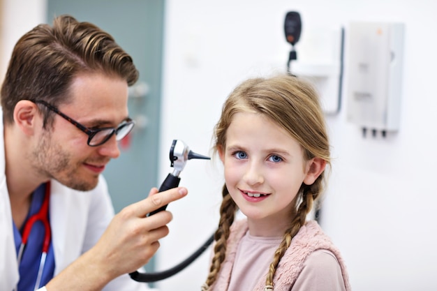 Médecin de sexe masculin examinant l'oreille de la fille avec un otoscope