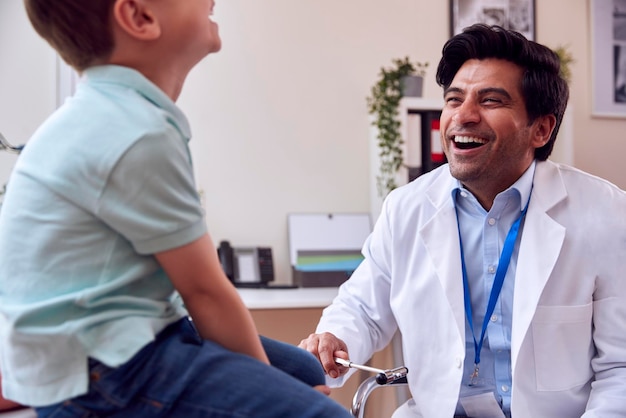 Médecin de sexe masculin ou généraliste portant un manteau blanc examinant un garçon souriant testant des réflexes