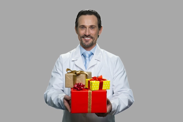 Médecin de sexe masculin heureux tenant de nombreux coffrets cadeaux. Bel homme en uniforme blanc offrant des coffrets cadeaux. Bonnes vacances d'hiver.