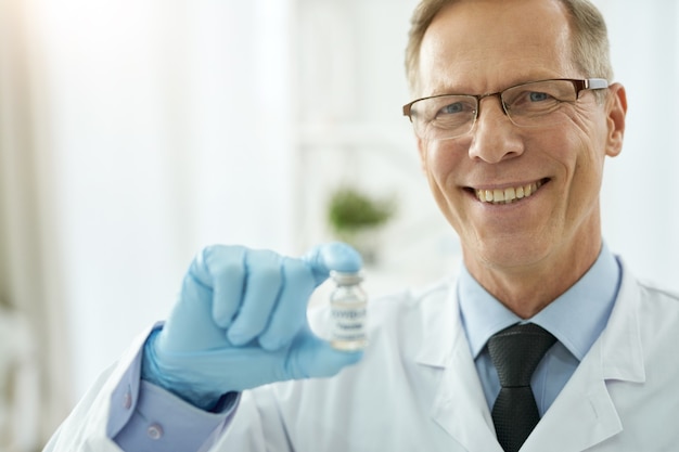 Médecin de sexe masculin joyeux tenant une bouteille de vaccin contre le covid