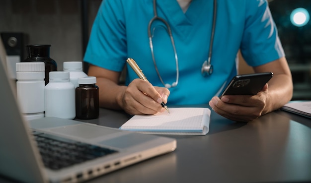 Médecin de sexe masculin médecin ou praticien en salle de laboratoire écrivant sur un cahier vierge et travaillant sur un ordinateur portable avec un stéthoscope médical sur le bureau à l'hôpital Medic tech concept