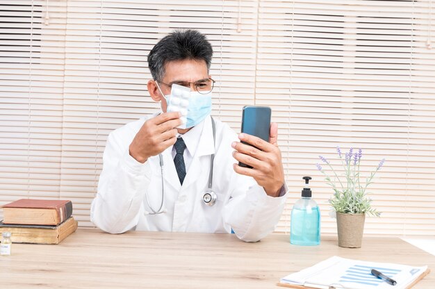 Un médecin de sexe masculin portant un masque organise un appel vidéo avec un patient pour lui donner des conseils.