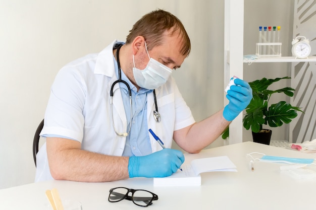 Un médecin de sexe masculin portant un masque de protection avec un stéthoscope tient une bouteille de vaccin à la main