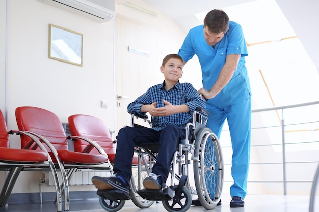 Médecin de sexe masculin prenant soin d'un petit garçon en fauteuil roulant à l'intérieur