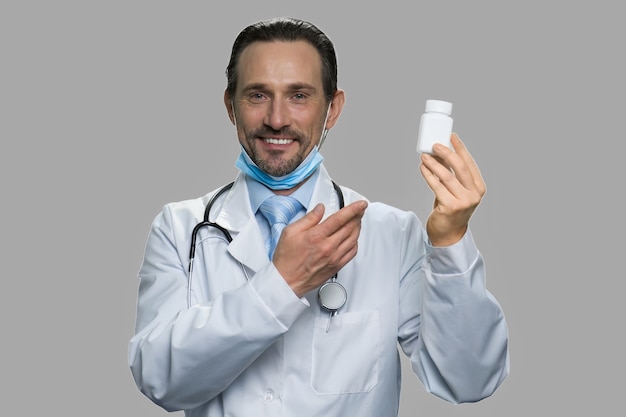 Médecin de sexe masculin présentant des pilules sur fond gris. Heureux médecin caucasien regardant la caméra.