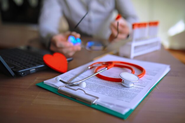 Médecin à son bureau dans le bureau de la clinique Tubes à essai pour stéthoscope Ordonnances pour ordinateur portable Lunettes sur la table