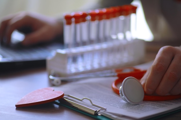 Médecin à son bureau dans le bureau de la clinique Tubes à essai pour stéthoscope Ordonnances pour ordinateur portable Lunettes sur la table