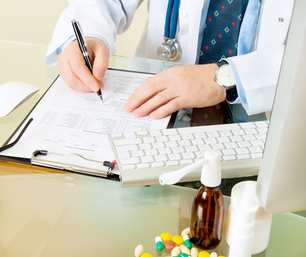 Photo médecin sur son lieu de travail avec ordinateur, pilules, comprimés