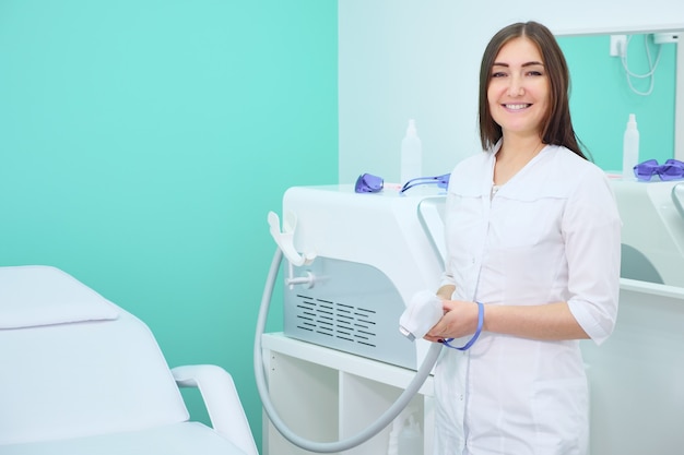 Médecin souriant en blouse blanche dans un salon de beauté d'épilation au laser et regardant la caméra