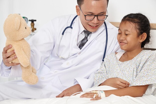 Photo un médecin souriant et une fille jouant avec un ours en peluche sur le lit à la maison