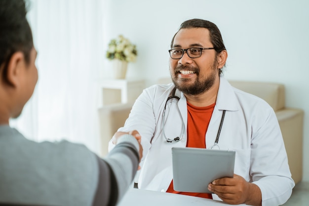 Médecin souriant, serrant la main du patient dans son bureau