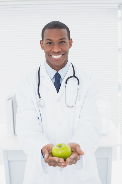 Médecin souriant tenant une pomme verte au cabinet médical