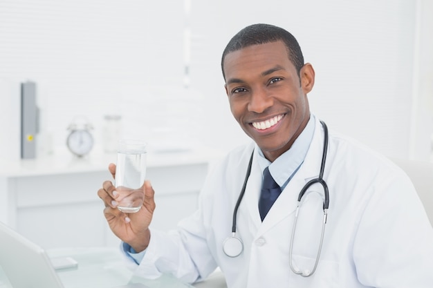 Médecin souriant tenant un verre d&#39;eau dans un cabinet médical