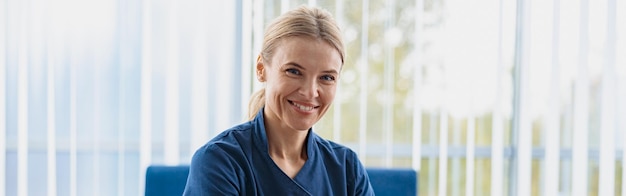 Médecin souriant travaillant sur un ordinateur portable lors d'un rendez-vous dans son cabinet médical et regardant la caméra