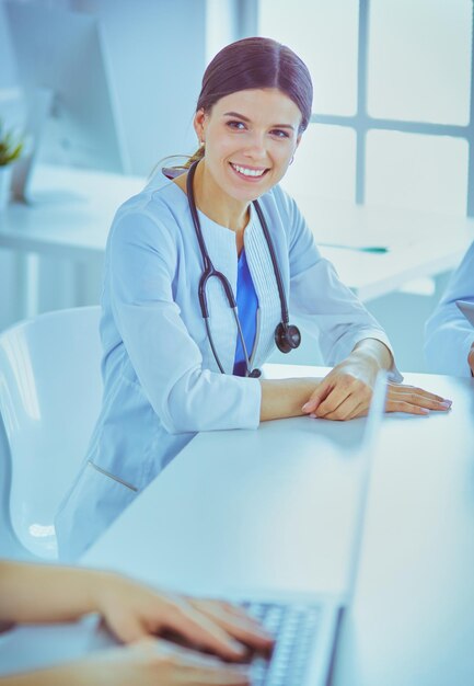Médecin souriant utilisant un ordinateur portable travaillant avec ses collègues dans une chambre d'hôpital lumineuse