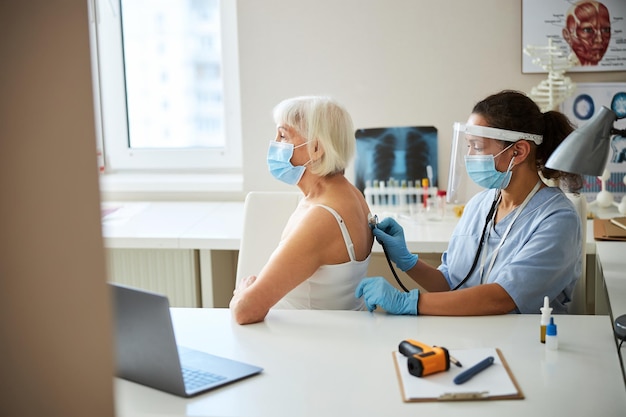 Médecin spécialiste à l'écoute d'une femme à la retraite respirant