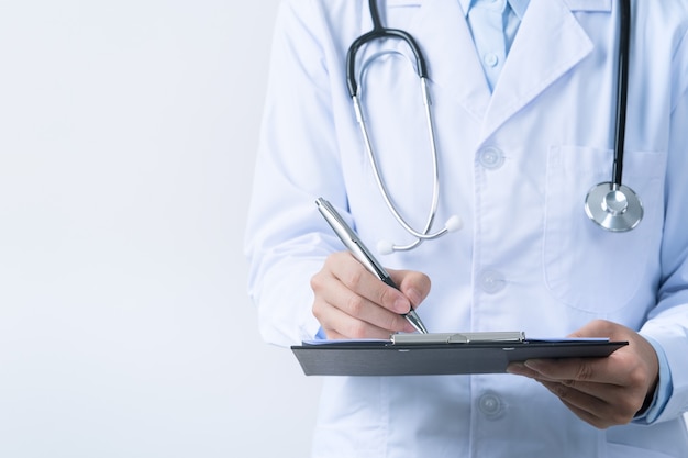 Médecin avec stéthoscope en blouse blanche tenant le presse-papiers, écrit le diagnostic de dossier médical, isolé sur fond blanc, gros plan, vue recadrée.