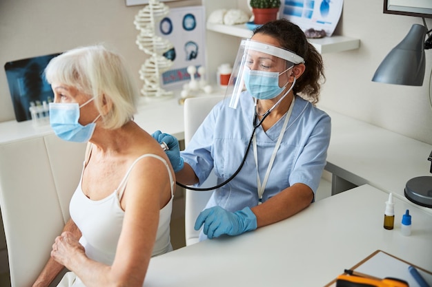 Médecin avec un stéthoscope entendant une vieille dame respirer