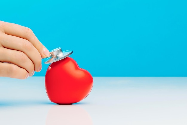 Un médecin avec stéthoscope examinant le coeur rouge isolé sur fond bleu