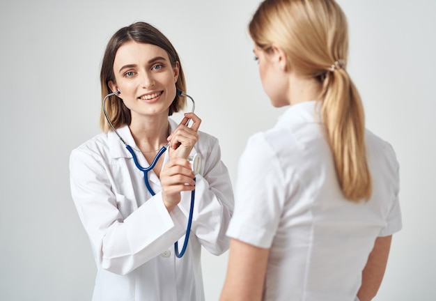 Un médecin avec un stéthoscope examine une femme en t-shirt blanc sur fond clair