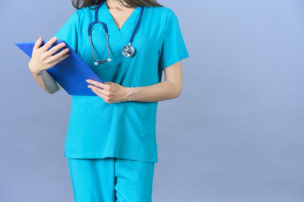 Médecin avec stéthoscope regardant un rapport médical avec un uniforme aigue-marine sur fond bleu