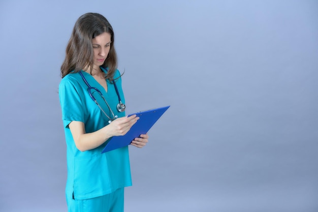 Médecin avec stéthoscope regardant un rapport médical avec un uniforme aigue-marine sur fond bleu